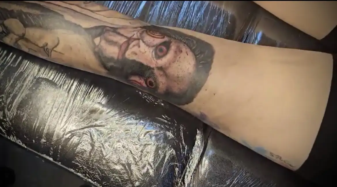 BL-ink Tattoo Colorado Springs forearm portrait: distressed red-eyed man in black-grey realism with subtle color highlights